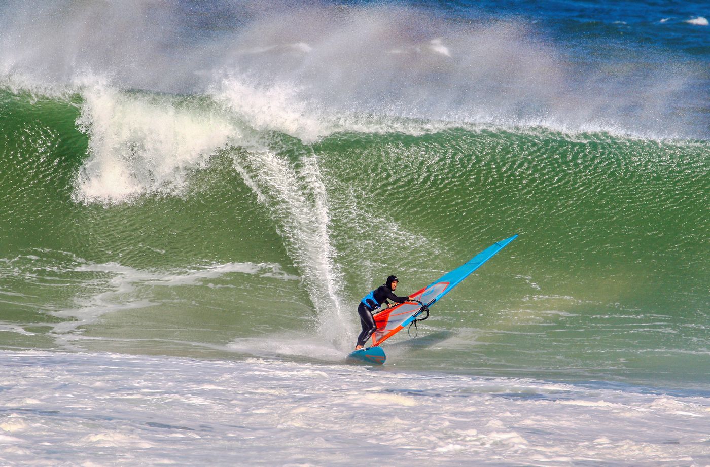 A male windsurfer carving across a powerful ocean wave